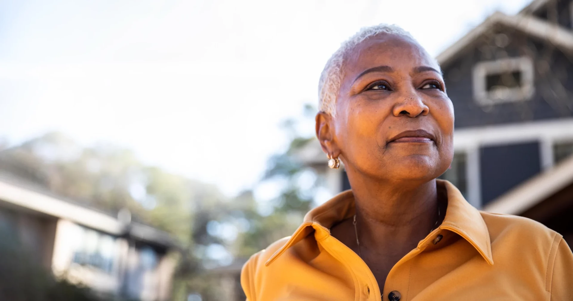 An older woman looking toward the horizon outside her home